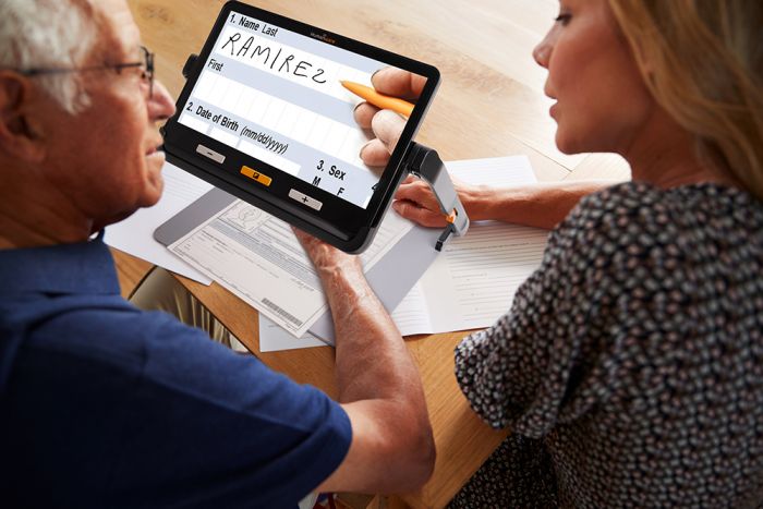 A woman helping her aging father filling out a paper form using the exploré 12 on the folding stand. 