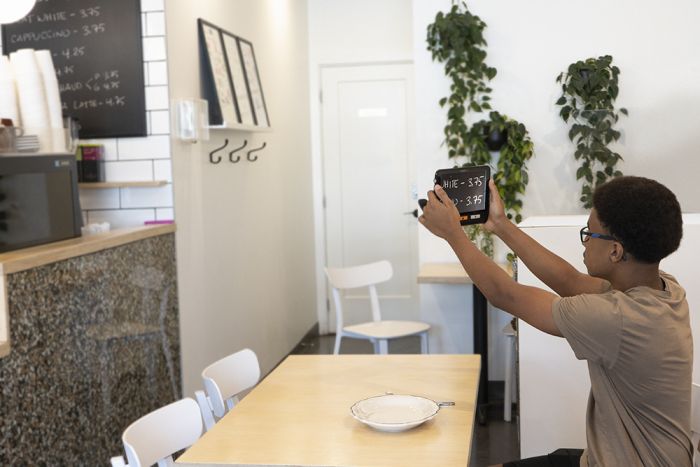 A teenager in a coffee shop uses the exploré 8 to look at the blackboard menu from a distance.