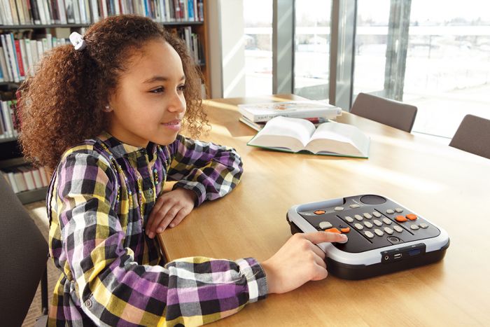 School-age girl using a Victor Reader Stratus12 M in a library.