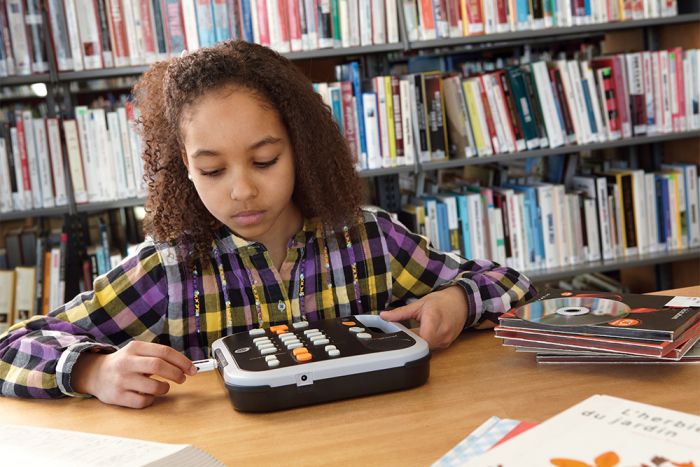 A schoolgirl in a library inserting a USB stick into a Victor Reader Stratus12 M.